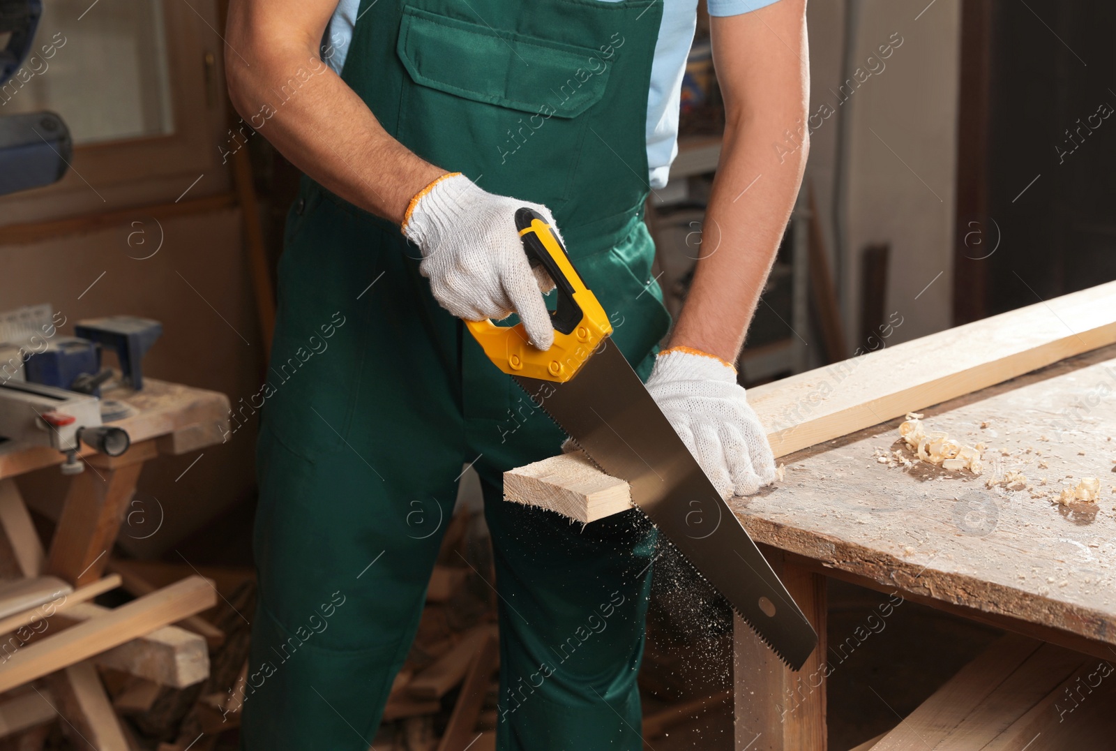 Photo of Professional carpenter cutting wooden board with handsaw in workshop, closeup