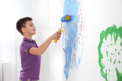 Photo of Little child painting wall with roller brush indoors