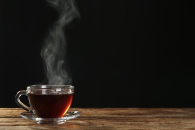 Photo of Cup with steam on wooden table against black background. Space for text