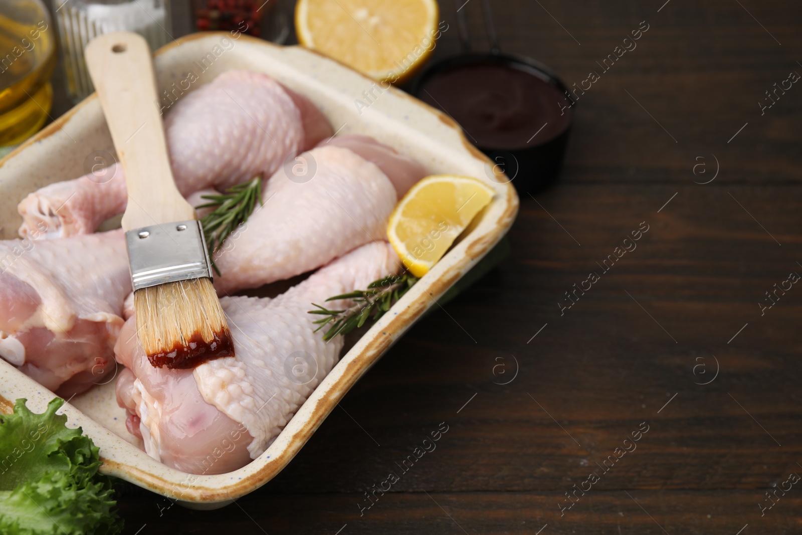 Photo of Basting brush with marinade, raw chicken drumsticks, rosemary and lemon on wooden table. Space for text