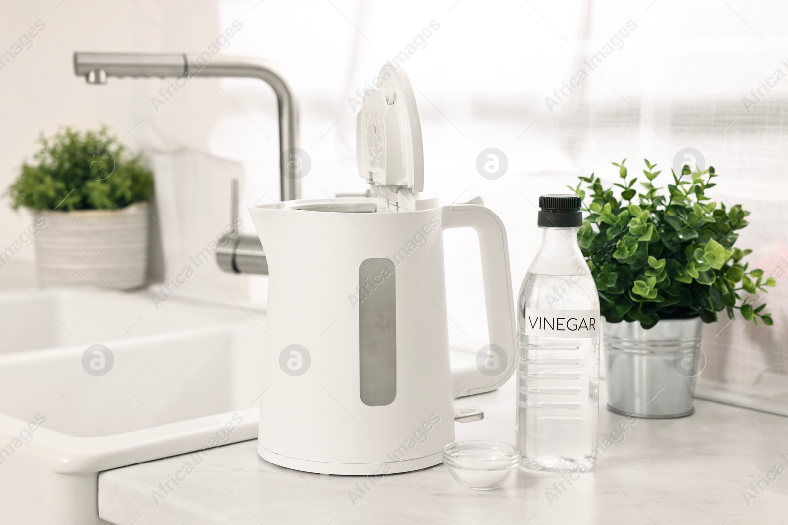 Photo of Cleaning electric kettle. Bottle of vinegar and baking soda on countertop in kitchen