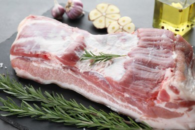 Photo of Piece of raw pork belly, rosemary and garlic on grey table, closeup