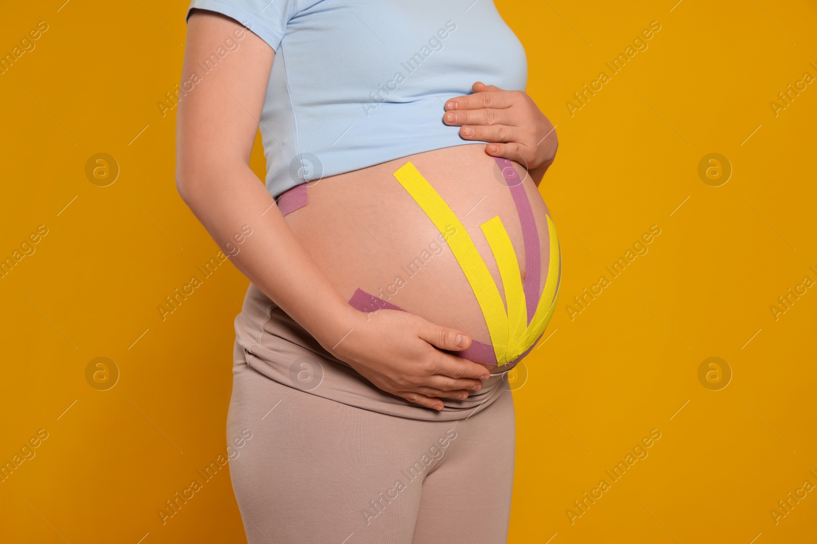 Photo of Pregnant woman with kinesio tapes on her belly against orange background, closeup