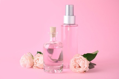 Bottles of essential oil and roses on pink background