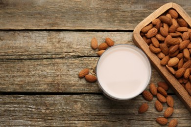 Glass of almond milk and almonds on wooden table, top view. Space for text