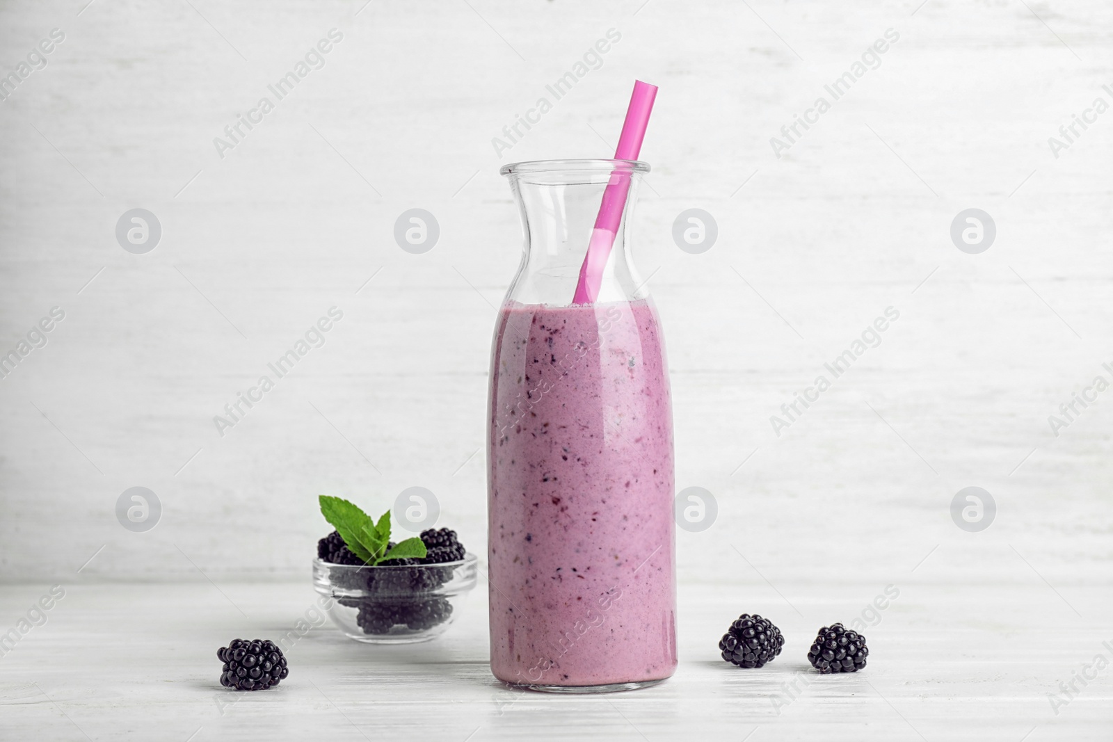 Photo of Delicious blackberry smoothie in bottle on white wooden table