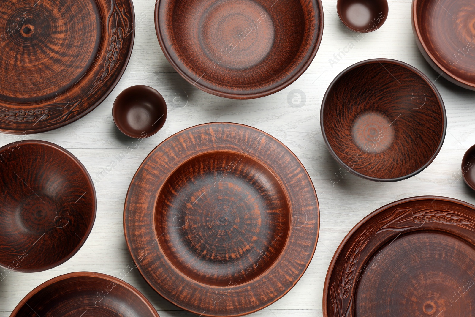 Photo of Set of clay utensils on white wooden table, flat lay