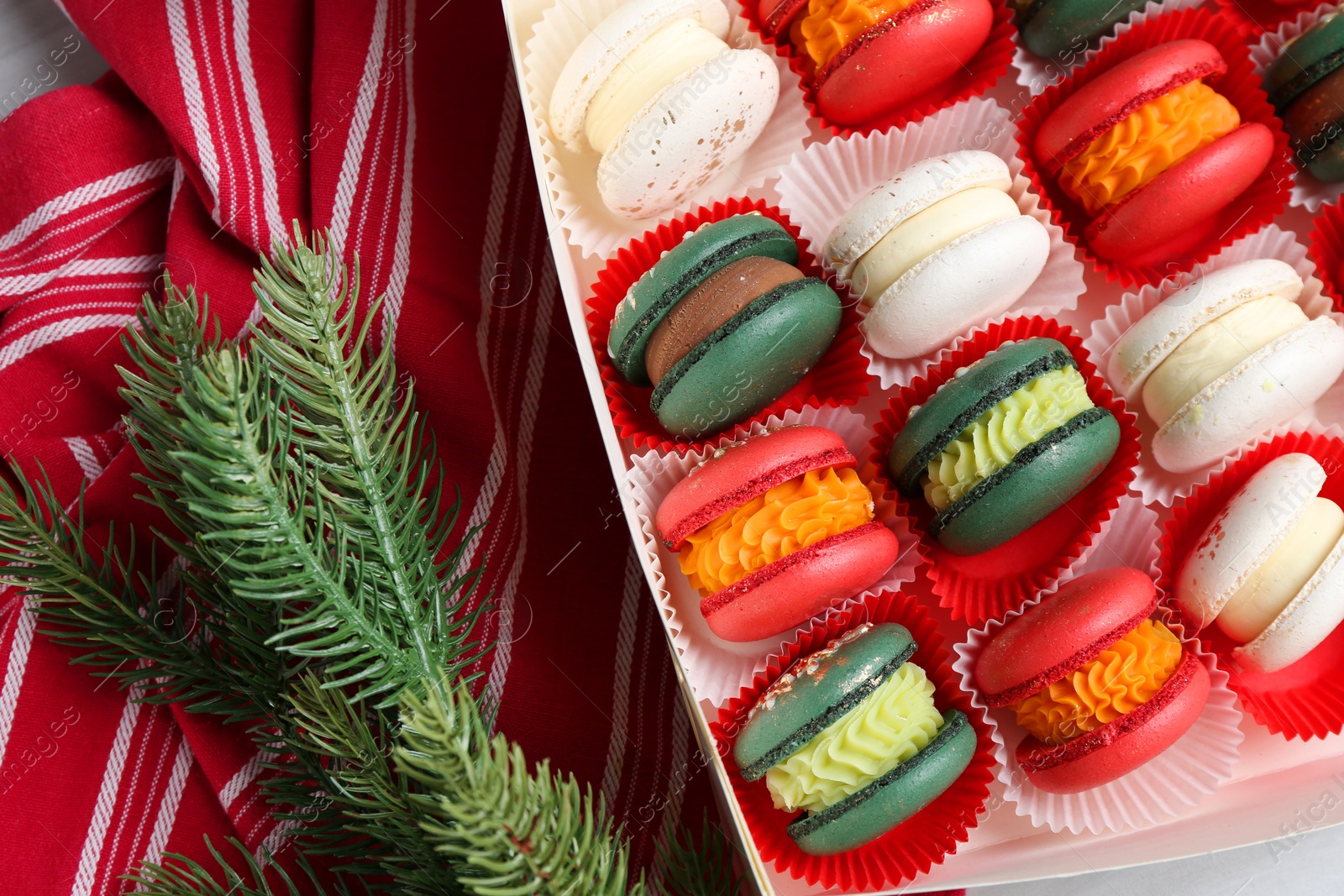 Photo of Different tasty Christmas macarons in box and fir branches on table, flat lay