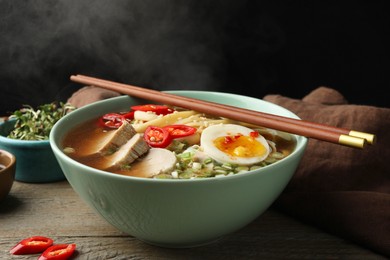 Delicious ramen in bowl on wooden table against black background, closeup. Noodle soup