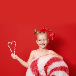 Cute little girl dressed as candy with sweets on red background. Christmas suit