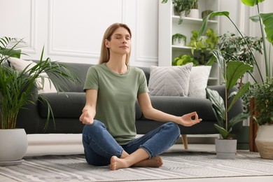 Woman meditating surrounded by beautiful potted houseplants at home