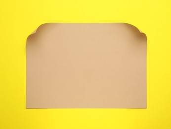 Sheet of brown paper on yellow background, top view