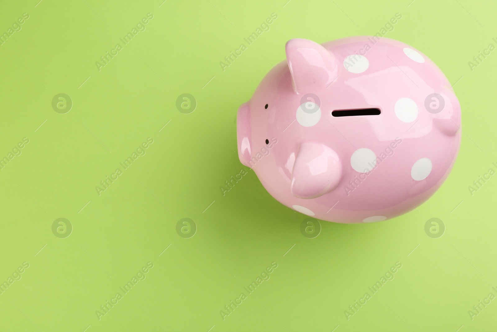 Photo of Pink piggy bank on green background, top view. Space for text