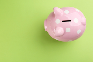 Photo of Pink piggy bank on green background, top view. Space for text