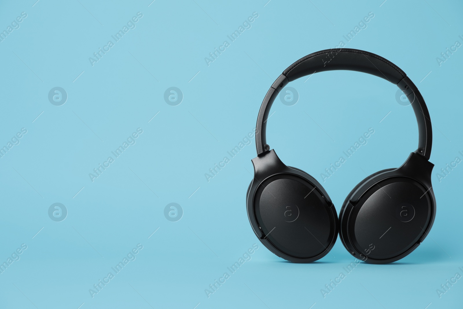 Photo of Modern wireless headphones on light blue background. Space for text