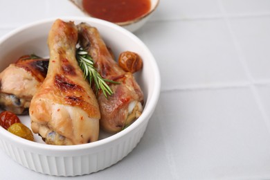 Photo of Marinade, roasted chicken drumsticks, rosemary and tomatoes on white tiled table, closeup. Space for text