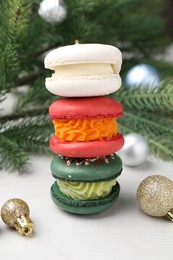 Photo of Stack of different decorated Christmas macarons and festive decor on white table, closeup