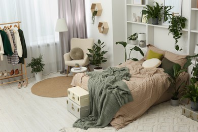 Photo of Stylish bedroom with comfortable bed, clothes rack and different houseplants. Interior design