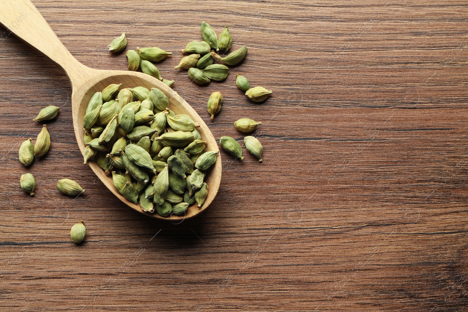 Photo of Spoon with dry cardamom pods on wooden table, top view. Space for text