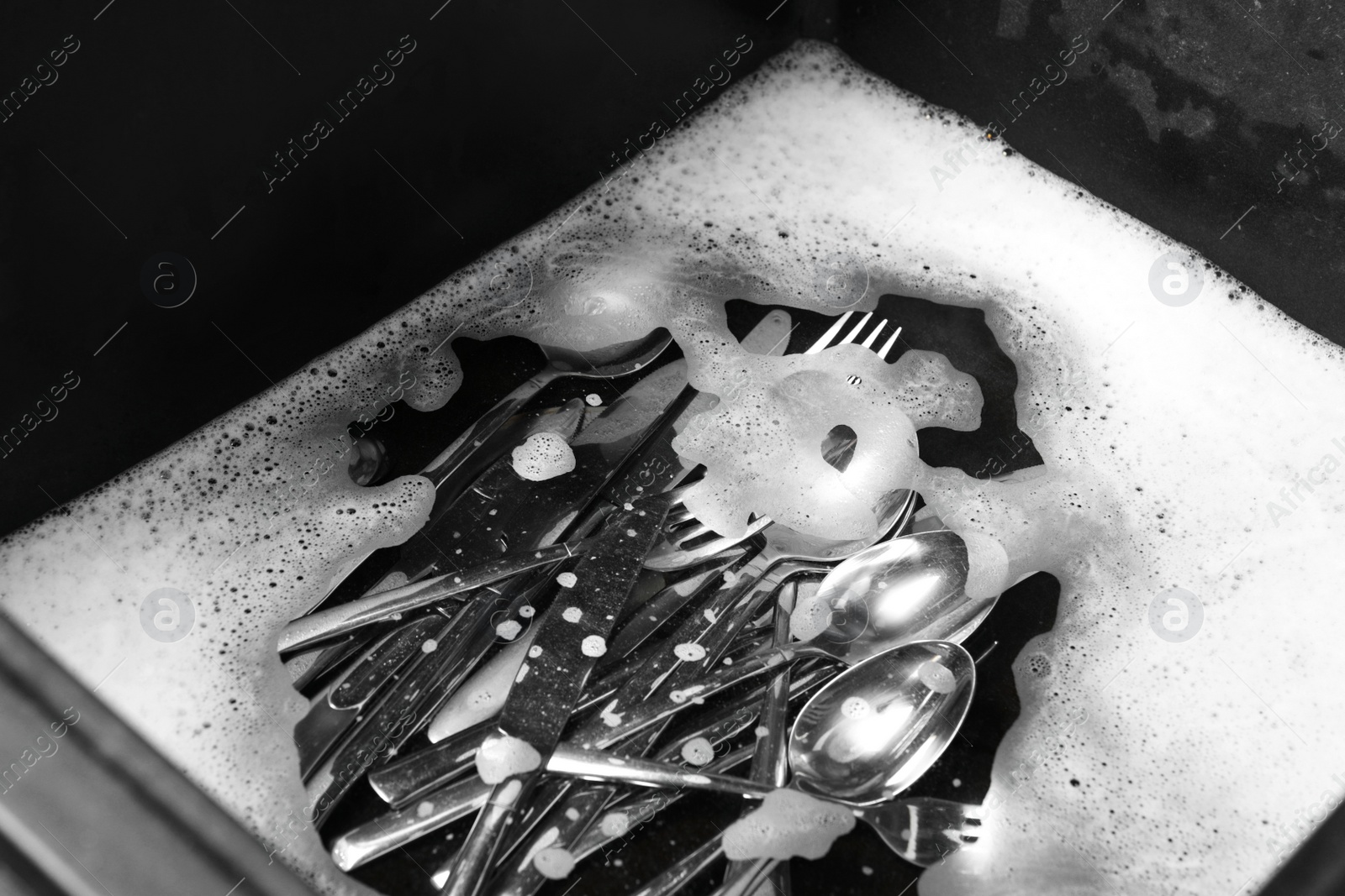 Photo of Washing silver spoons, forks and knives in kitchen sink with foam, above view