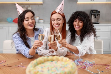 Happy young women clinking glasses of sparkling wine at birthday party in kitchen