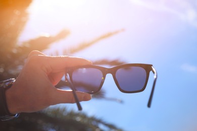 Mature man holding stylish sunglasses outdoors on sunny day, closeup