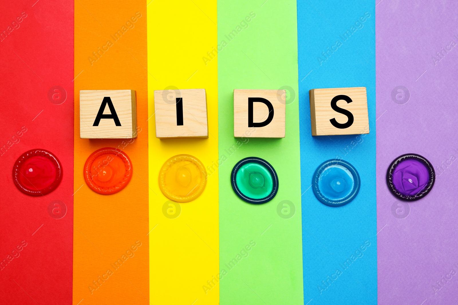 Photo of Word AIDS made with wooden cubes and colorful condoms on rainbow background, flat lay. Safe sex