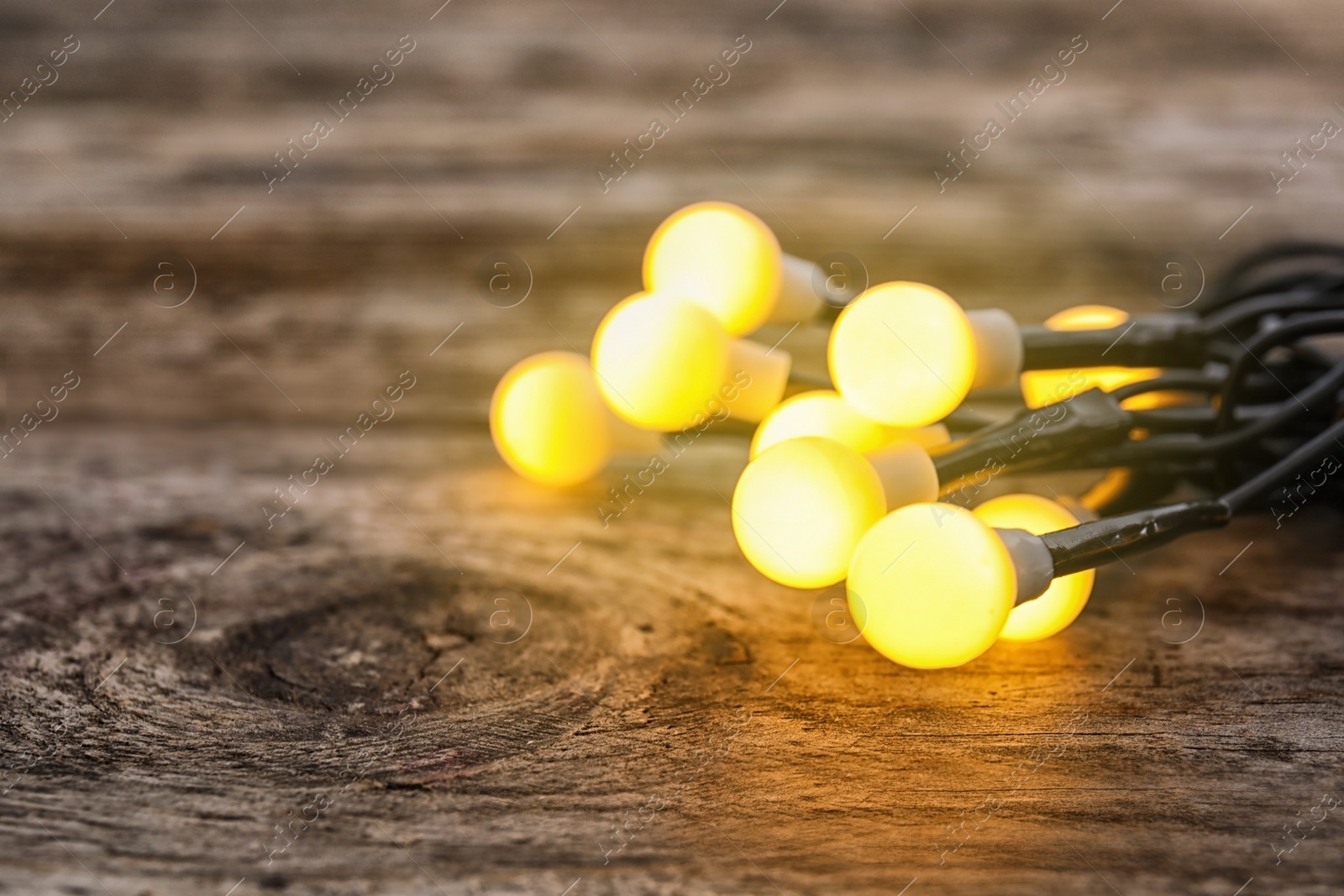 Photo of Glowing Christmas lights on wooden table, closeup