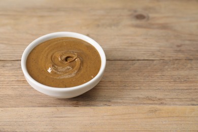 Delicious nut butter in bowl on wooden table, closeup. Space for text