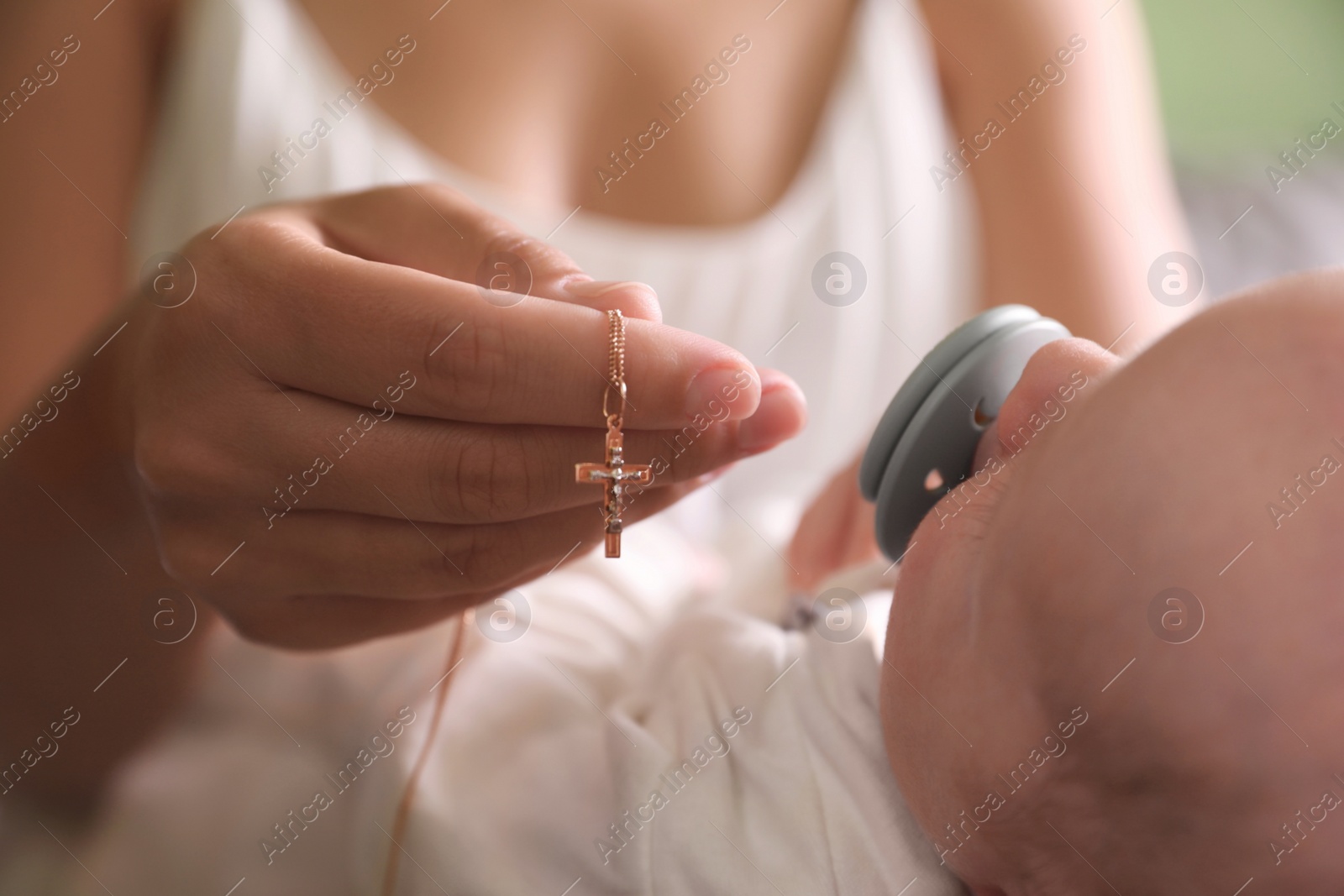 Photo of Mother holding Christian cross near newborn baby indoors, closeup