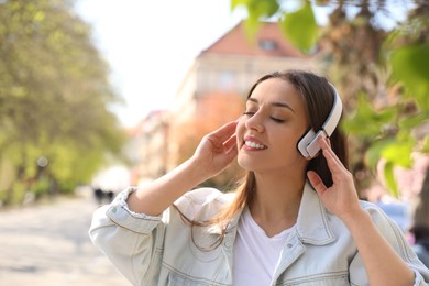 Photo of Young woman with headphones listening to music outdoors, space for text