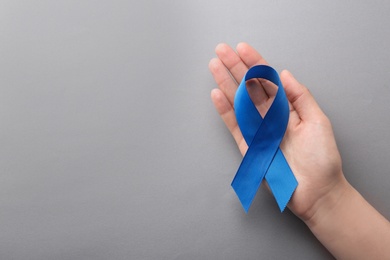 Photo of Woman holding blue awareness ribbon on grey background, top view with space for text. Symbol of social and medical issues