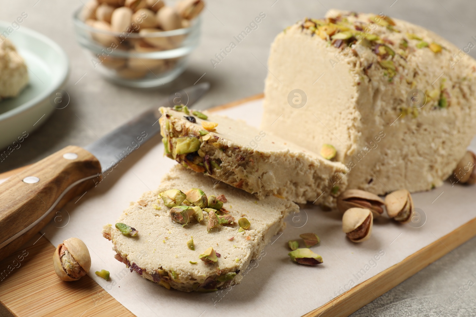 Photo of Tasty halva with pistachios and knife on grey table, closeup