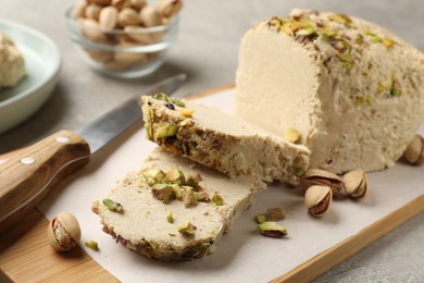 Photo of Tasty halva with pistachios and knife on grey table, closeup