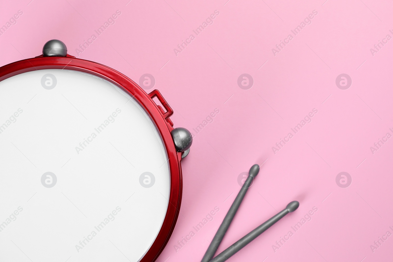 Photo of Children's drum with drumsticks on pink background, top view. Space for text