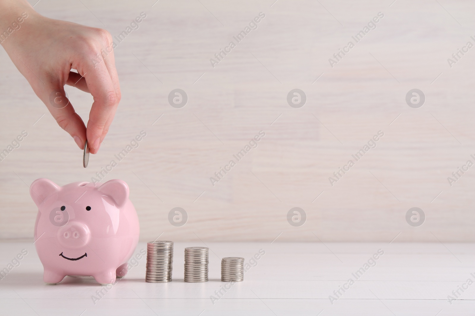 Photo of Financial savings. Woman putting coin into piggy bank at white wooden table, closeup. Space for text