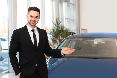 Photo of Young salesman near new car in dealership