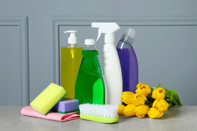 Photo of Spring cleaning. Detergents, flowers and tools on grey textured table