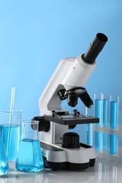 Different laboratory glassware, test tubes with light blue liquid and microscope on table