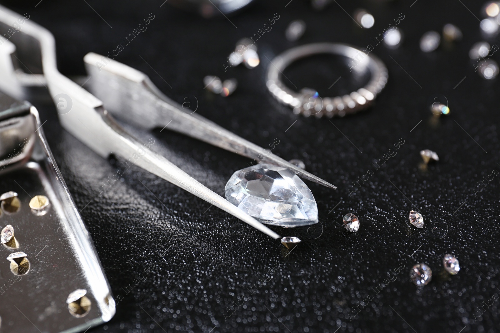 Photo of Jewels and tweezers on black leather surface