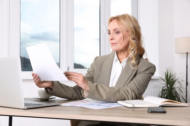 Photo of Lady boss with papers working near laptop at desk in office. Successful businesswoman
