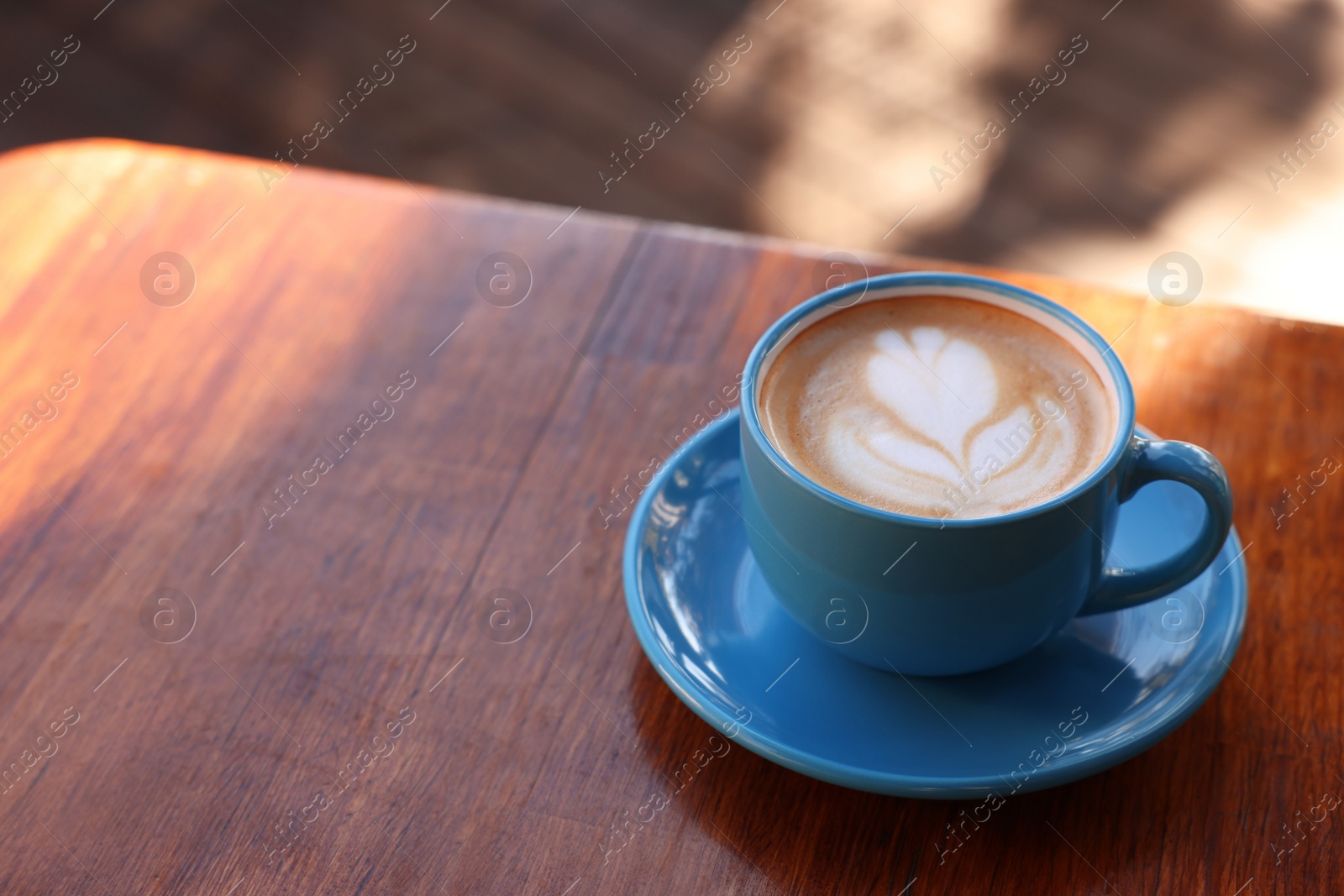 Photo of Ceramic cup of aromatic coffee with foam on wooden table in outdoor cafe. Space for text