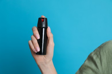 Photo of Young woman using pepper spray on turquoise background, closeup