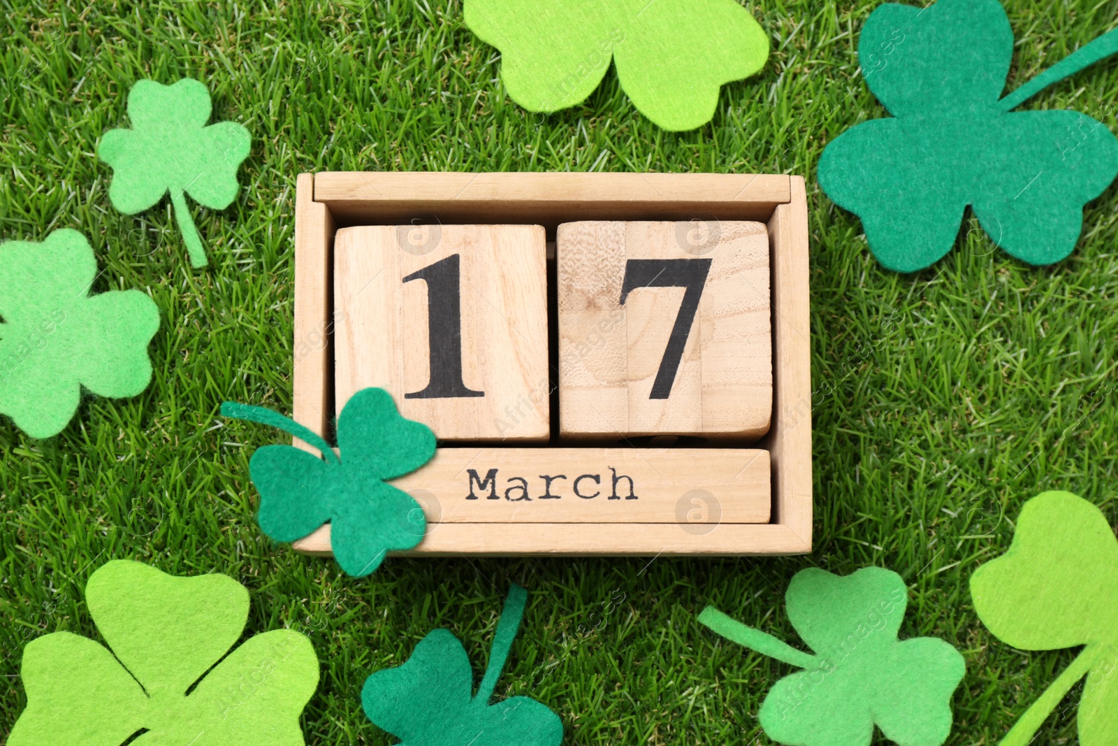 Photo of St. Patrick's day - 17th of March. Wooden block calendar and felt clover leaves on green grass, flat lay