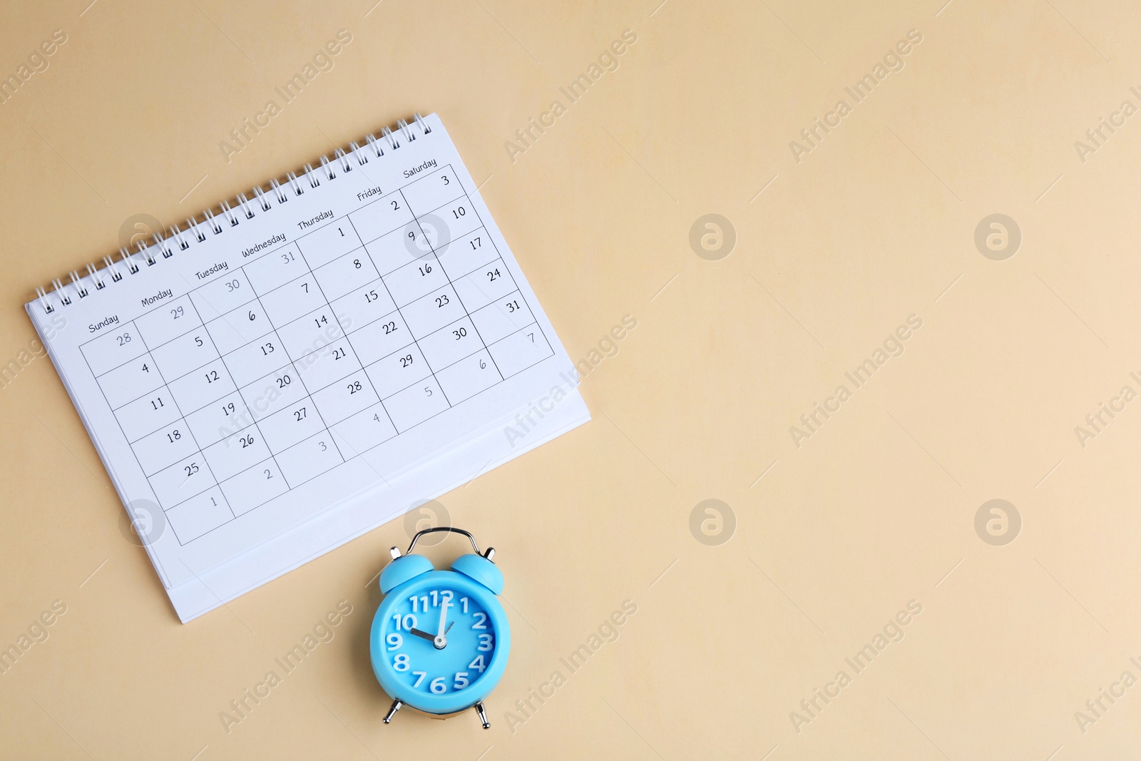 Photo of Calendar and alarm clock on beige background, flat lay. Space for text