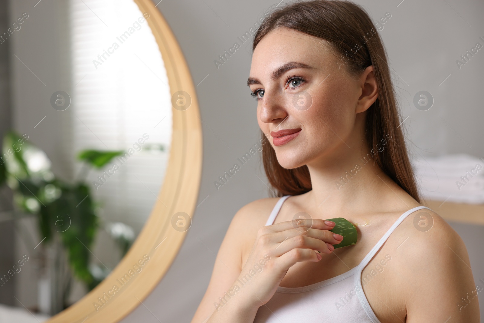 Photo of Young woman applying aloe gel from leaf onto her shoulder in bathroom. Space for text