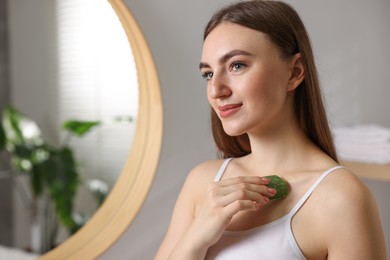 Photo of Young woman applying aloe gel from leaf onto her shoulder in bathroom. Space for text