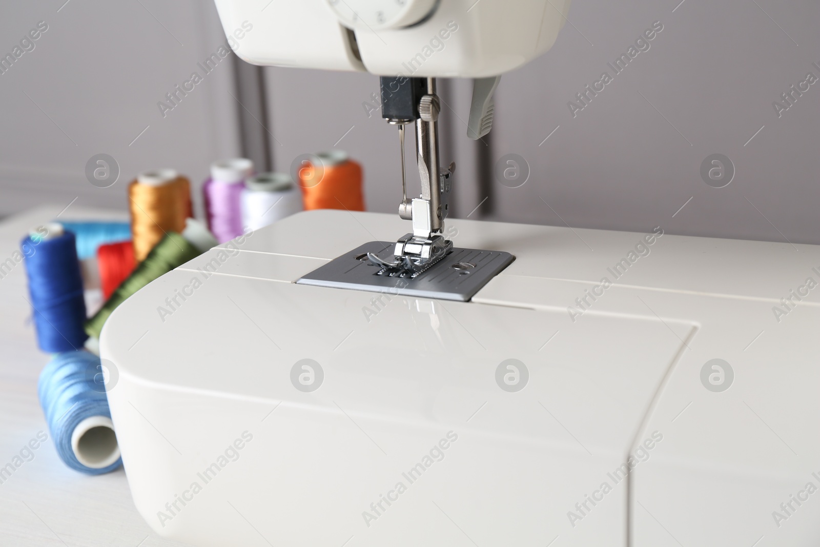 Photo of Sewing machine and spools of threads on white table indoors, closeup