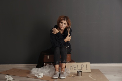 Photo of Poor homeless woman asking for help near dark wall