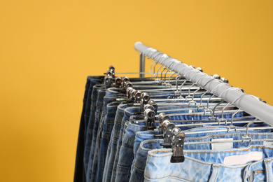 Rack with different jeans on yellow background